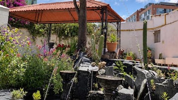 Un jardín con una fuente, palmeras y una estructura de techo rojo.