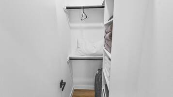 A narrow hallway with a white door, a white shelf with folded towels, and a white bench with a towel draped over it.