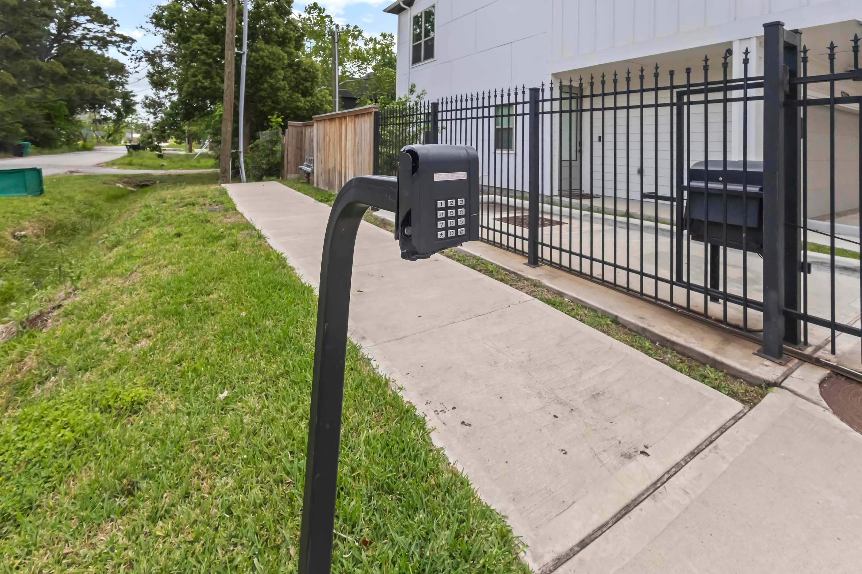 A mailbox on a sidewalk next to a black metal fence.