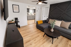 A modern living room with a dark sofa, a coffee table, and a television. - Historic Loft - 1 Medcenter NRG DT Fifa (Houston)