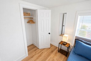 Ein Zimmer mit Holzboden, einer weißen Tür, einem kleinen Tisch mit Lampe und einem blauen Sofa.