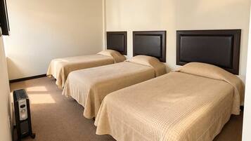 A room with three beds, each with a headboard, a heater, and a wall-mounted television.