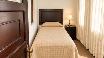 A hotel room with a bed, a nightstand with a lamp, a door, and curtains.