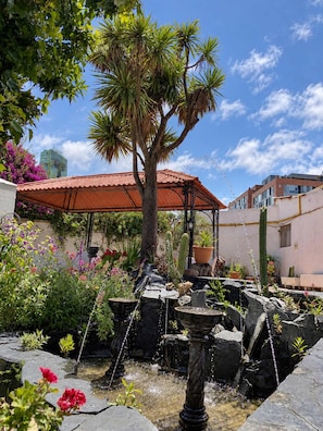 A garden with a fountain, palm trees, and a red-roofed structure. - Calacoto Secret Garden 3BR Zona Sur Parking (La Paz)