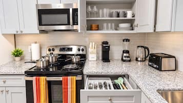 A modern kitchen with white cabinets, a stainless steel stove, a microwave, a toaster, a blender, and a coffee maker.