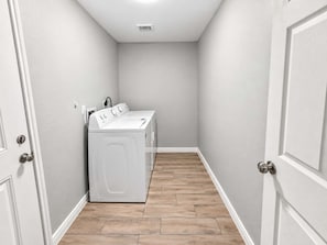 A laundry room with a washing machine and dryer, white walls, and wooden flooring. - Spacious 4BR I Private Backyard Sleeps 8 I Near NRG Med Center DT (Houston)