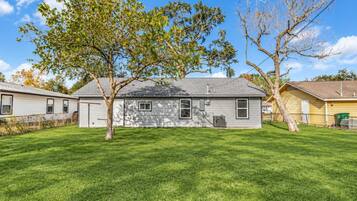 A single-story house with a sloped roof, a front yard, and a tree in the center.