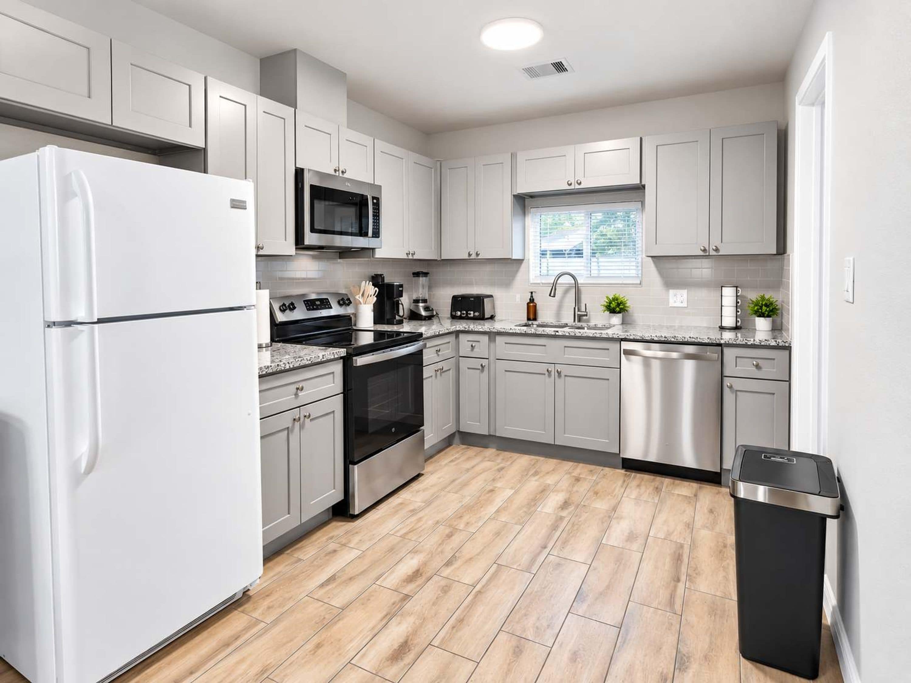 A modern kitchen with white cabinets, stainless steel appliances, and a wooden floor.