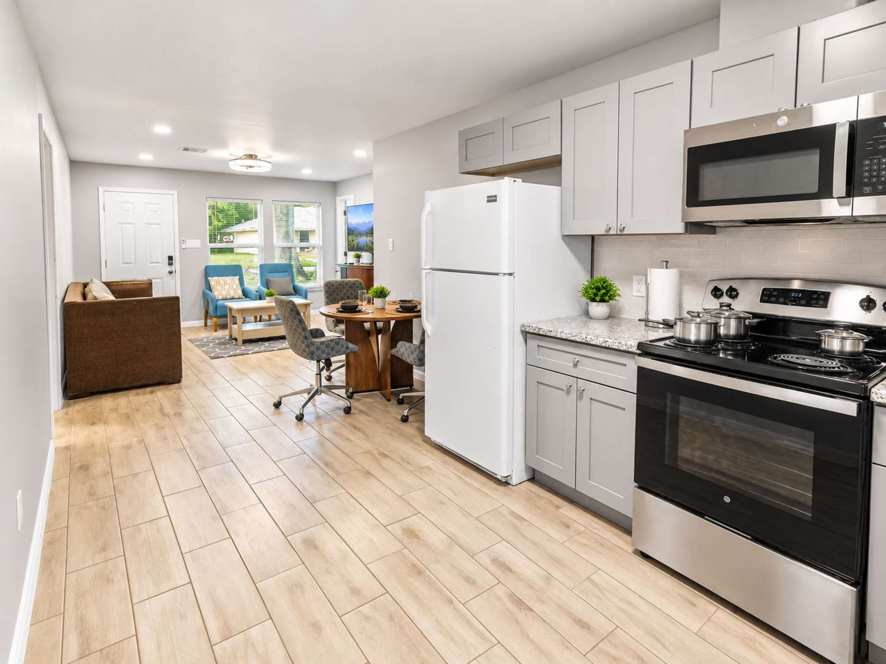A modern kitchen with stainless steel appliances, a dining area with a table and chairs, and a view of the outdoors.