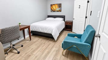A small, neatly arranged bedroom with a bed, a desk, a chair, and a door.