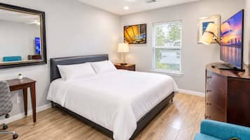 A hotel room with a bed, a desk, a chair, a dresser, a mirror, a ceiling fan, and artwork on the walls.