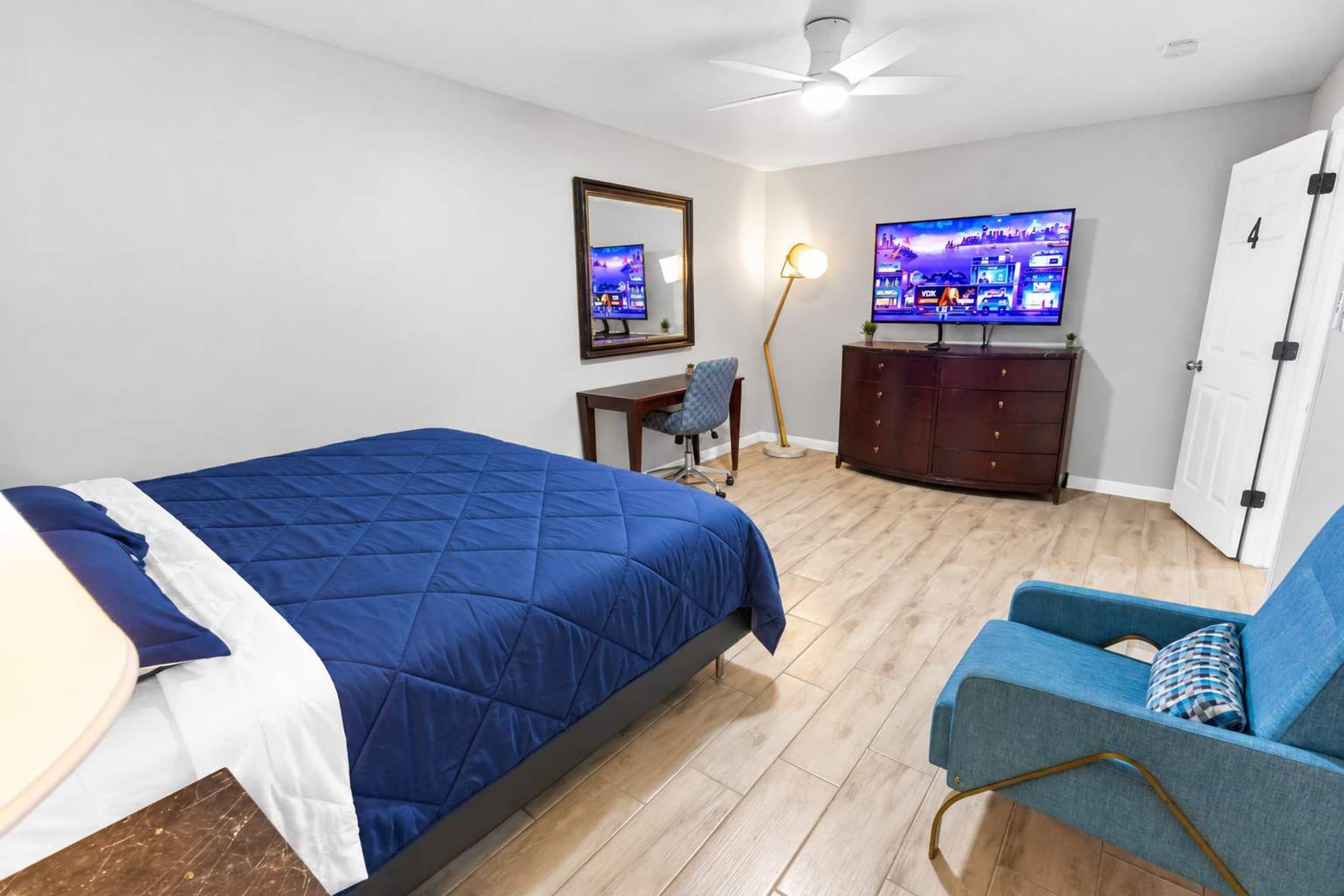 Un dormitorio con cama, escritorio, silla, cómoda, televisor y puerta.
