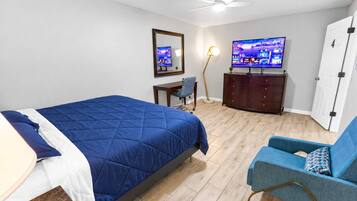 Un dormitorio con cama, escritorio, silla, cómoda, televisor y puerta.