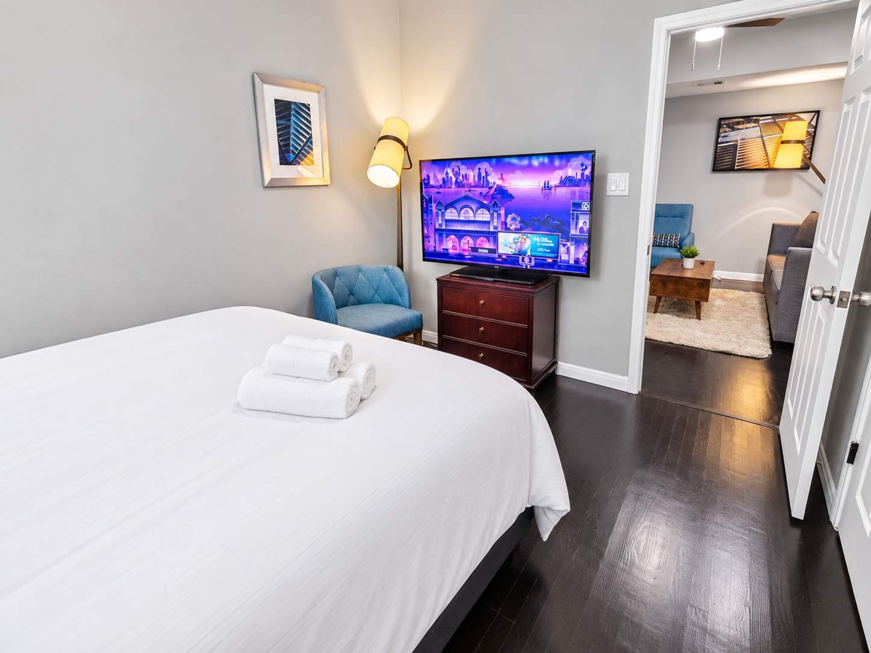 Hotellihuone, jossa on sänky, televisio, tuoli ja työpöytä, jossa on lamppu.