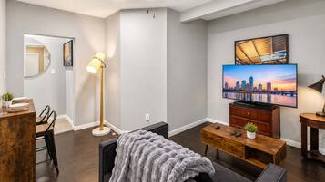 Una sala de estar moderna con un televisor de pantalla plana montado en la pared, una mesa de centro de madera, un sofá gris y una lámpara de pie.