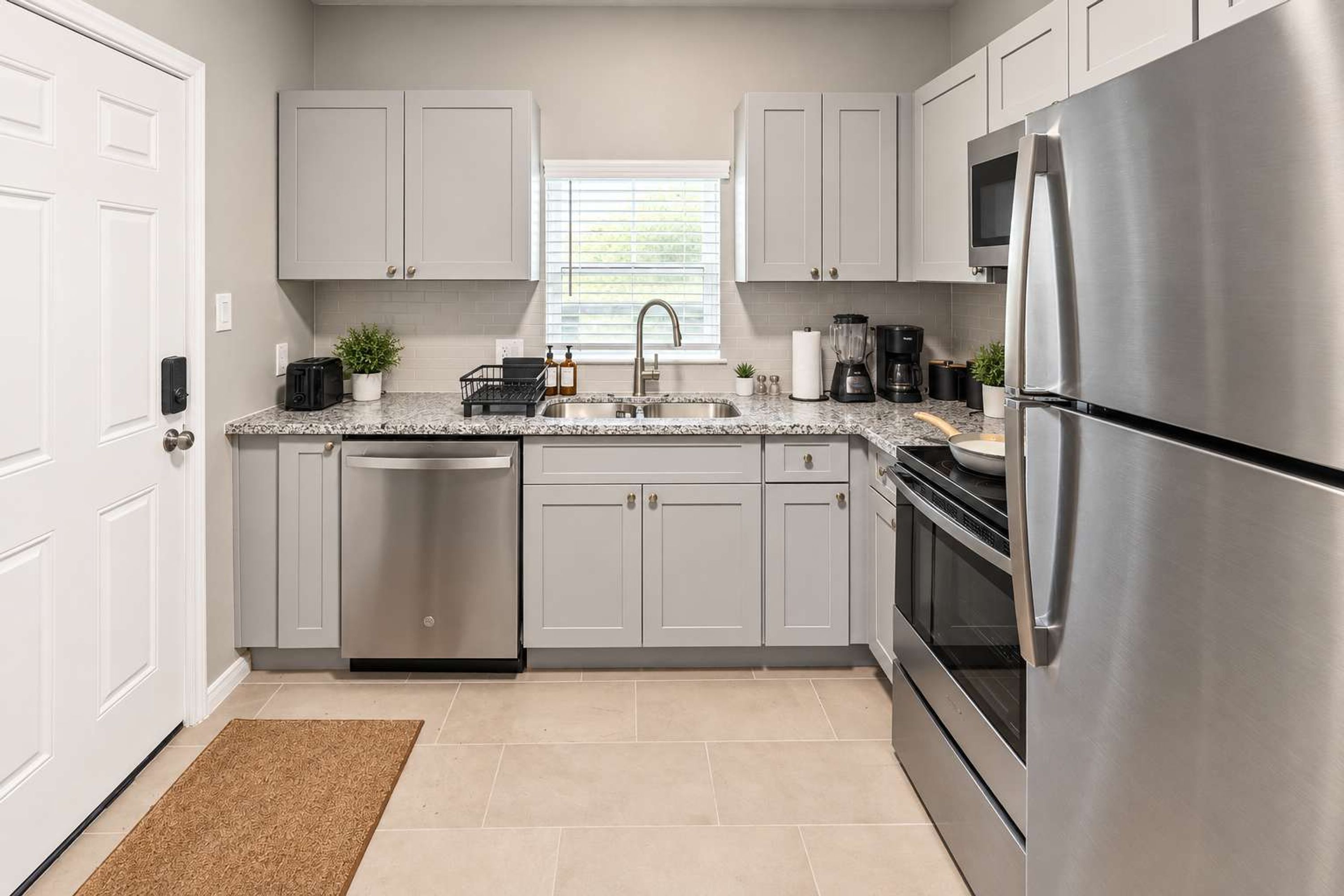 A modern kitchen with stainless steel appliances, white cabinetry, and a window providing natural light.