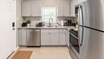 A modern kitchen with stainless steel appliances, white cabinetry, and a window providing natural light.