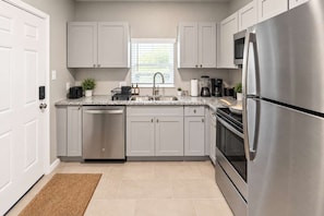 A modern kitchen with stainless steel appliances, white cabinetry, and a window providing natural light. - Fifa Stay 2BR Near NRG DT Med Center -4 (Houston)