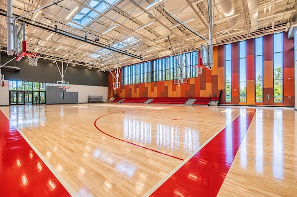 A basketball court with a wooden floor and red lines, large windows, and a high ceiling with visible ductwork. - Fifa Stay 2BR Near NRG DT Med Center -3 (Houston)