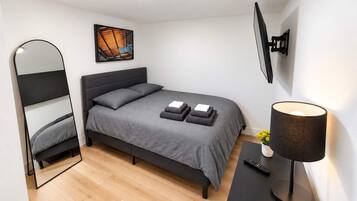 A modern bedroom with a bed, a bedside table, a lamp, a mirror, and a painting on the wall.