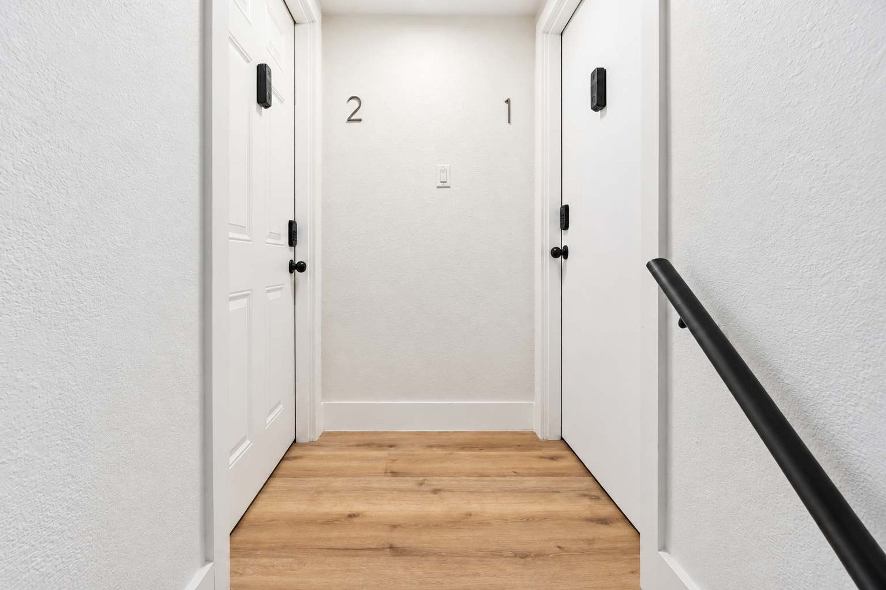 A narrow hallway with wooden flooring and white walls, leading to a door marked with the number 2.