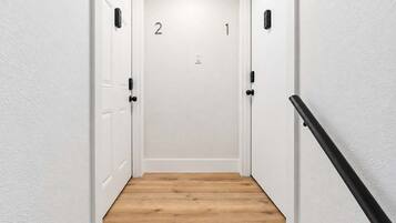 A narrow hallway with wooden flooring and white walls, leading to a door marked with the number 2.