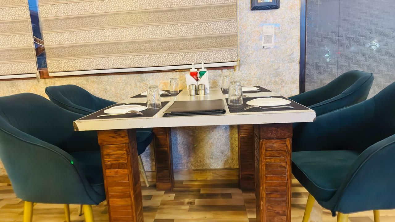 Un espace repas avec une table rectangulaire dressée pour quatre personnes, entourée de chaises à l’assise rembourrée de couleur vert foncé.