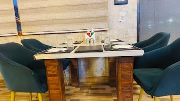 Un espace repas avec une table rectangulaire dressée pour quatre personnes, entourée de chaises à l’assise rembourrée de couleur vert foncé.