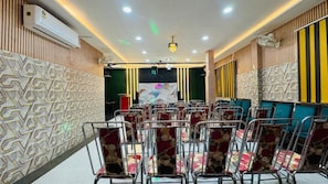 A conference room with rows of chairs, a stage with a backdrop, and a ceiling with recessed lighting.