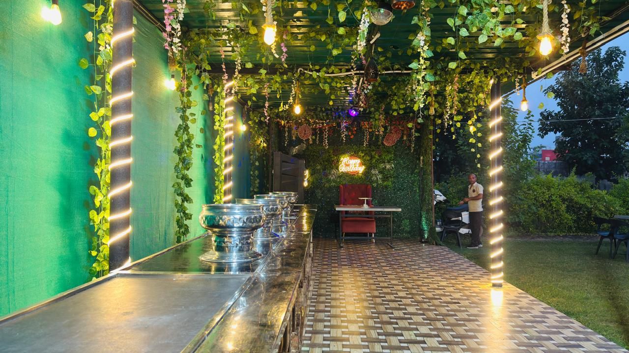 An outdoor dining area with a long table, hanging plants, and string lights.