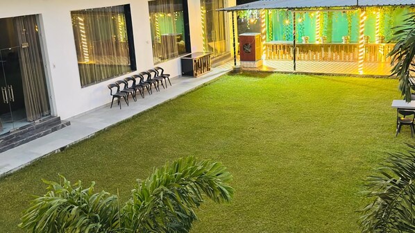 Un patio con césped artificial, mobiliario exterior y zona de bar con guirnaldas de luces.