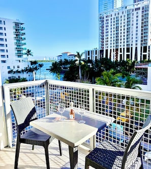 A balcony with a table and chairs, overlooking a cityscape with tall buildings and palm trees. - Midtown Wynwood 2 bedroom condo w/h free parking (Miami)