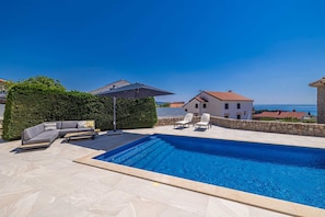 A swimming pool with lounge chairs and a sofa, surrounded by stone walls and a hedge. - Villa SIA With Private Pool (Krk)