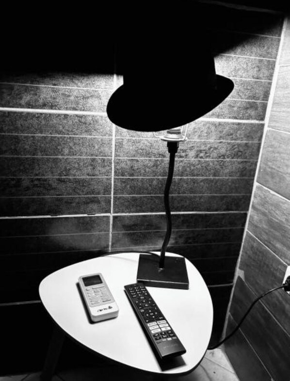 Uma mesa branca com uma lâmpada, um controle remoto e um celular.