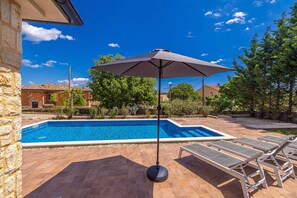 A swimming pool with a tiled deck, a lounge area with sun loungers, and a large umbrella providing shade. - Holiday House Casa DI Bronzo With Private Pool (Krk)