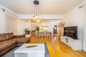 A spacious living room with a brown leather sofa, a white coffee table with a decorative item, a flat-screen TV on a white stand, and a dining area with a white table and chairs. - Holiday House Casa DI Bronzo With Private Pool (Krk)