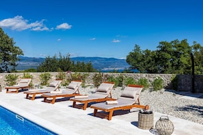 A poolside area with lounge chairs and a stone wall. - Luxury Villa Glabrova With Pool Jacuzzi and Sauna (Dobrinj)