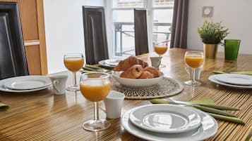 Une table en bois dressée pour le petit-déjeuner, avec des croissants, du jus d’orange et une plante verte.
