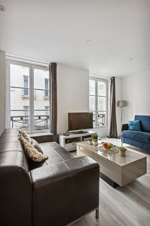Een moderne woonkamer met een bank, salontafel, televisie en uitzicht op een balkon.