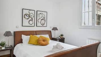 Una camera da letto ordinata con un letto di legno, biancheria bianca e due opere d'arte astratte appese alle pareti.