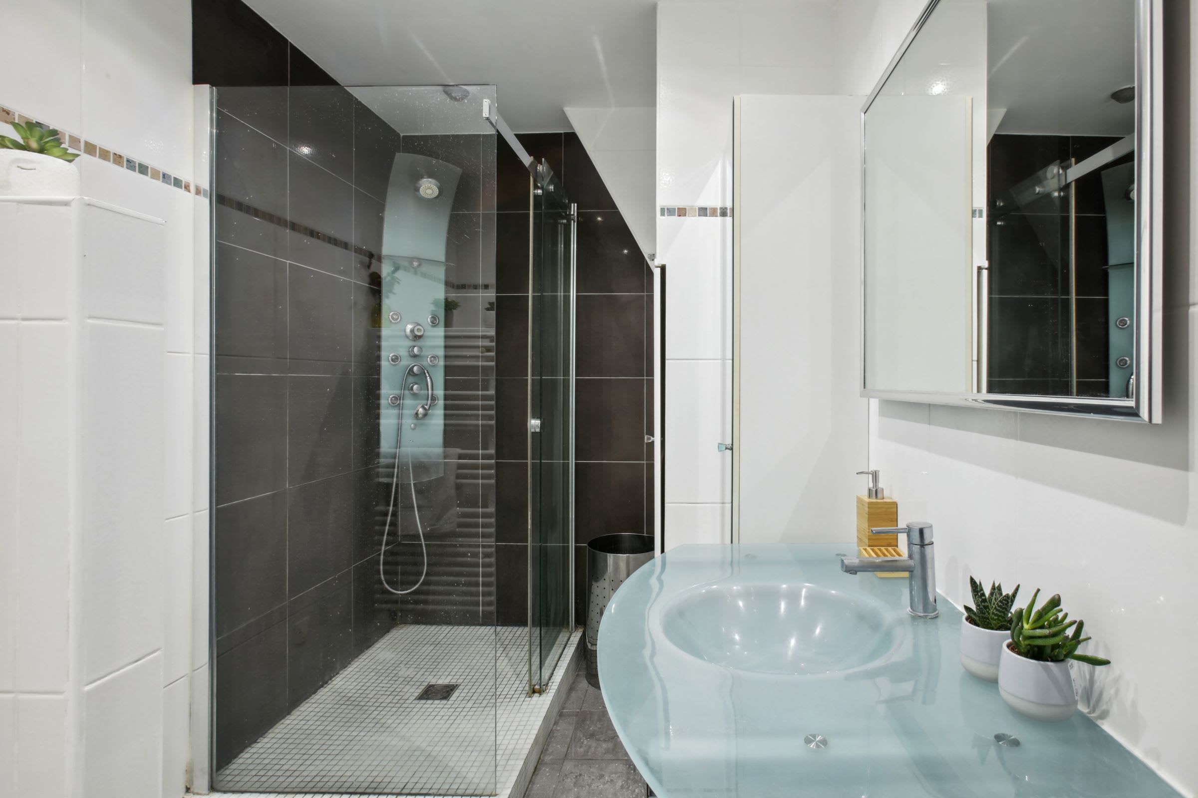 Ein modernes Badezimmer mit einer gläsernen Dusche, einem großen Glaswaschbecken und einem Spiegel darüber.
