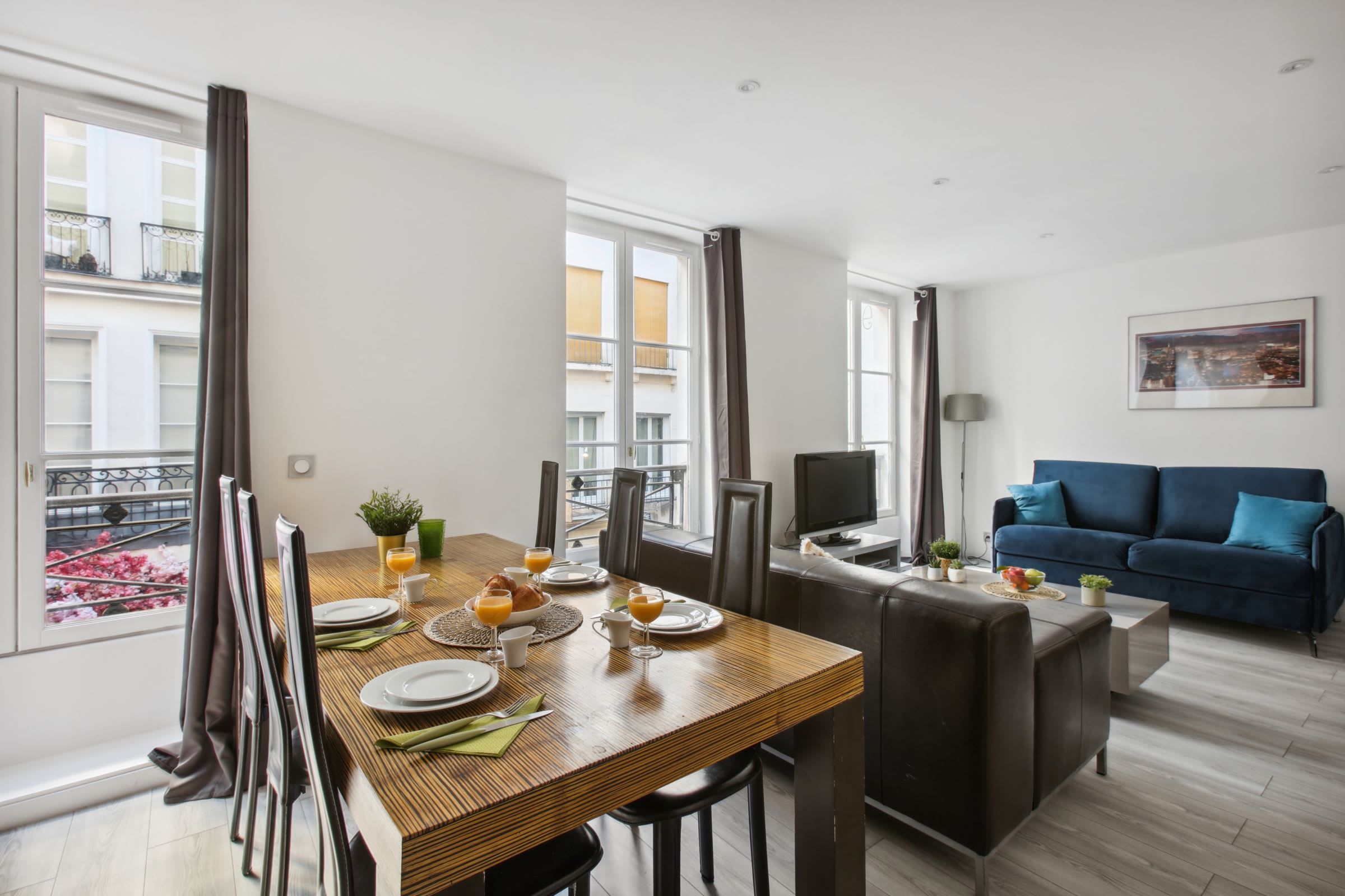Een moderne woonkamer met een eethoek, een blauwe bank en een televisie.