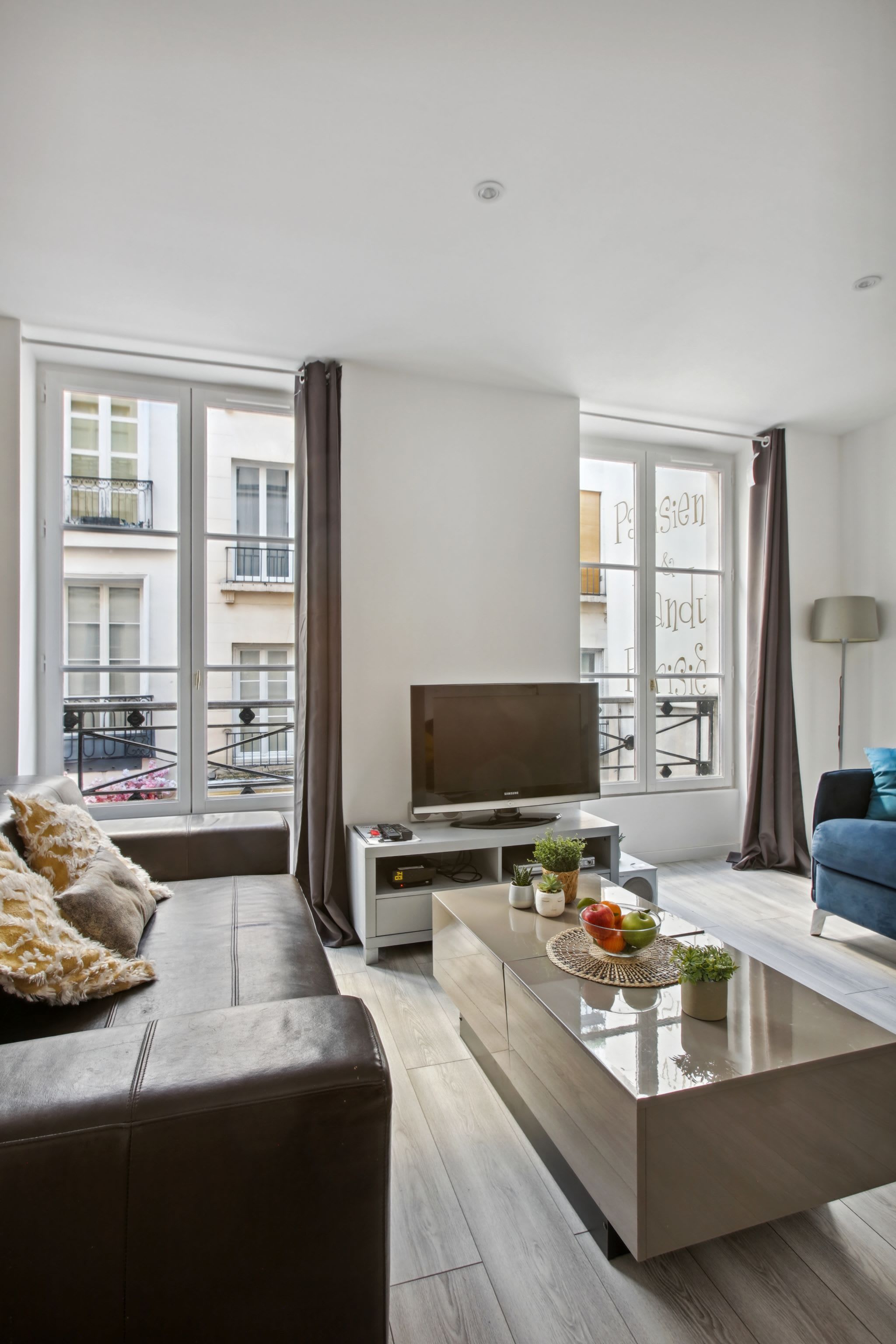 Un salon moderne comprenant un canapé, une table basse agrémentée d’objets décoratifs, un téléviseur et de grandes fenêtres avec des rideaux.