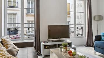 Un salon moderne comprenant un canapé, une table basse agrémentée d’objets décoratifs, un téléviseur et de grandes fenêtres avec des rideaux.