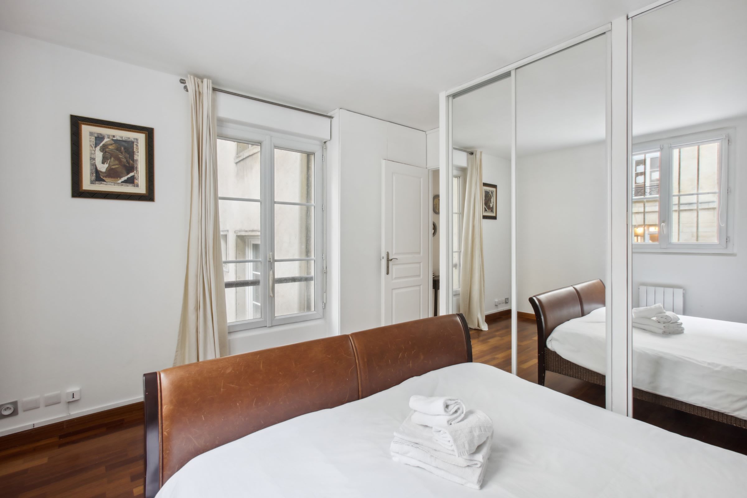 Een hotelkamer met een bed, een stoel, een spiegel en een raam met gordijnen.