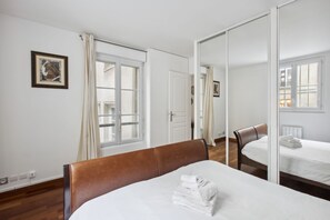 Een hotelkamer met een bed, een stoel, een spiegel en een raam met gordijnen.