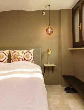 A bedroom with a bed, pillows, a nightstand, a lamp, and a shoe rack.