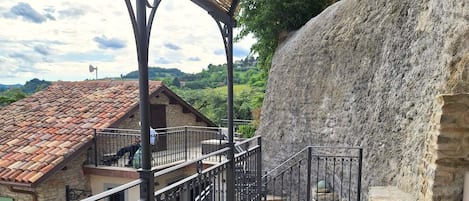 A covered outdoor seating area with a table and chairs, a stone wall, and a view of the surrounding landscape.