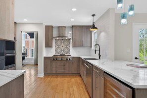 A modern kitchen with a central island, wooden cabinets, and a patterned backsplash. - Huge 4BR Game Retreat · Sleeps 8 · Chicago (Glendale Heights)