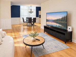 Ein Wohnzimmer mit einem großen Flachbildfernseher, einem Essbereich mit Tisch und Stühlen sowie einem Sofa.